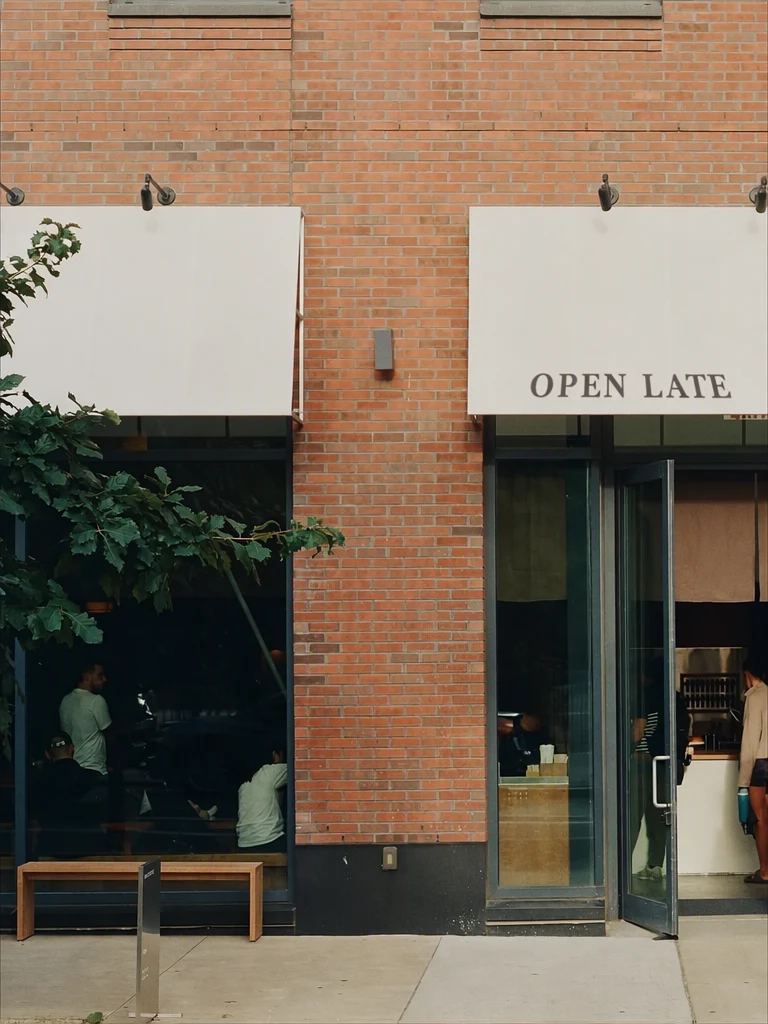The same cafe front with OPEN LATE printed in dark serif capitals on the right-hand awning