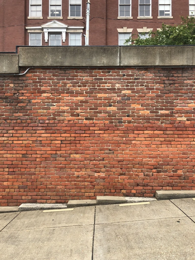 Red brick wall along a sloped sidewalk, with a brick building behind