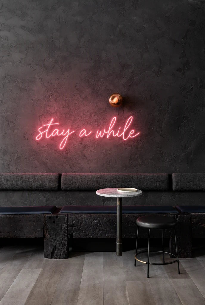 The same wall with a pink neon sign reading stay a while, glowing onto the plaster and the seats