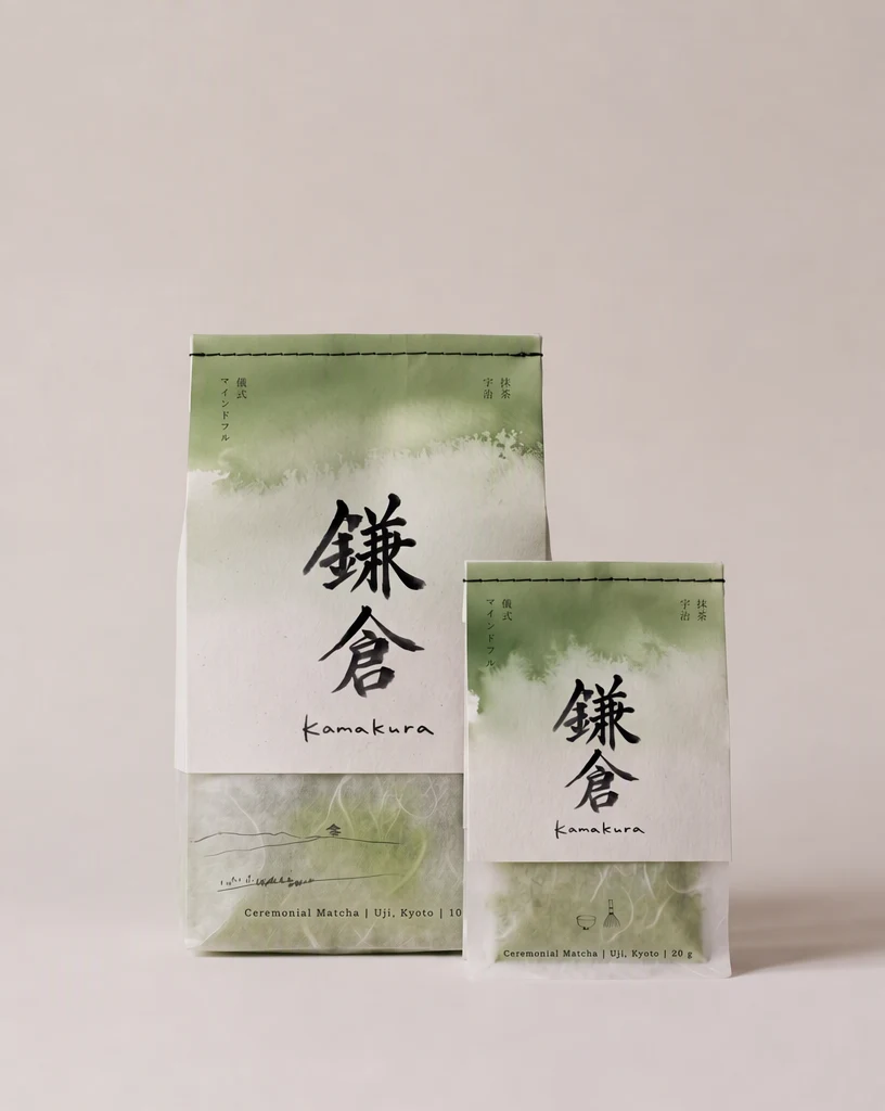 Les deux mêmes sachets avec le premier caractère au pinceau corrigé : la marque se lit 鎌倉 (Kamakura) dans le même style de pinceau noir ; le petit texte vertical, le nom en cursive et les lignes en anglais sont inchangés.