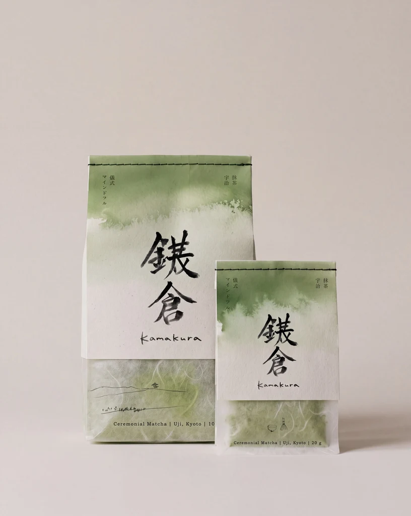 Emballages de matcha générés par IA : un grand et un petit sachet en papier avec le haut en aquarelle verte, la marque écrite en grands kanji noirs au pinceau avec un premier caractère mal formé, « Kamakura » en écriture cursive en dessous, et un petit texte japonais vertical.